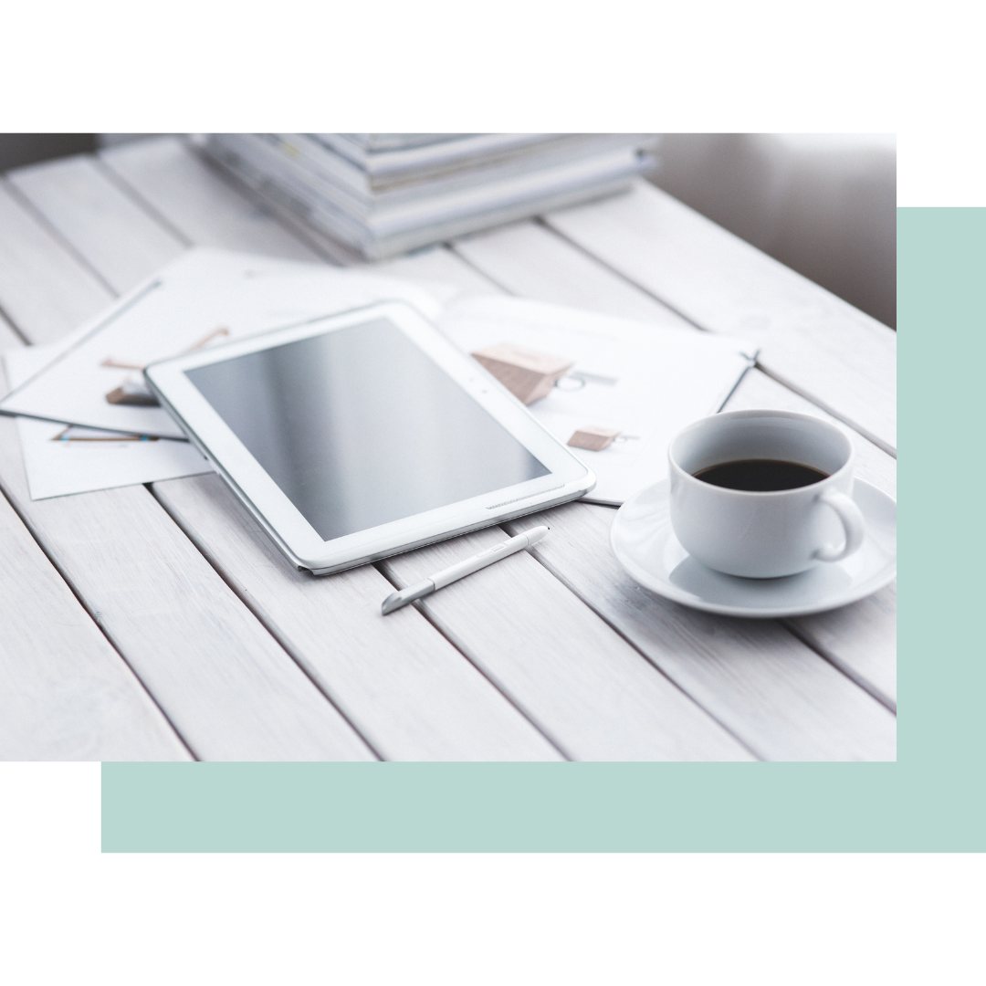 Tablet, papirer og en kop kaffe på et hvidt bord